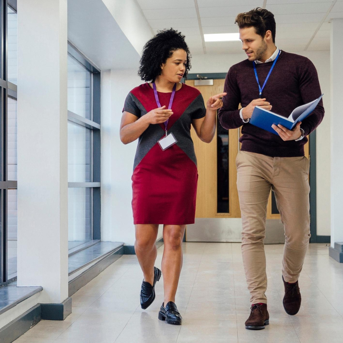 Two educators, a man and a woman, have a conversation walk down the hallway. 
