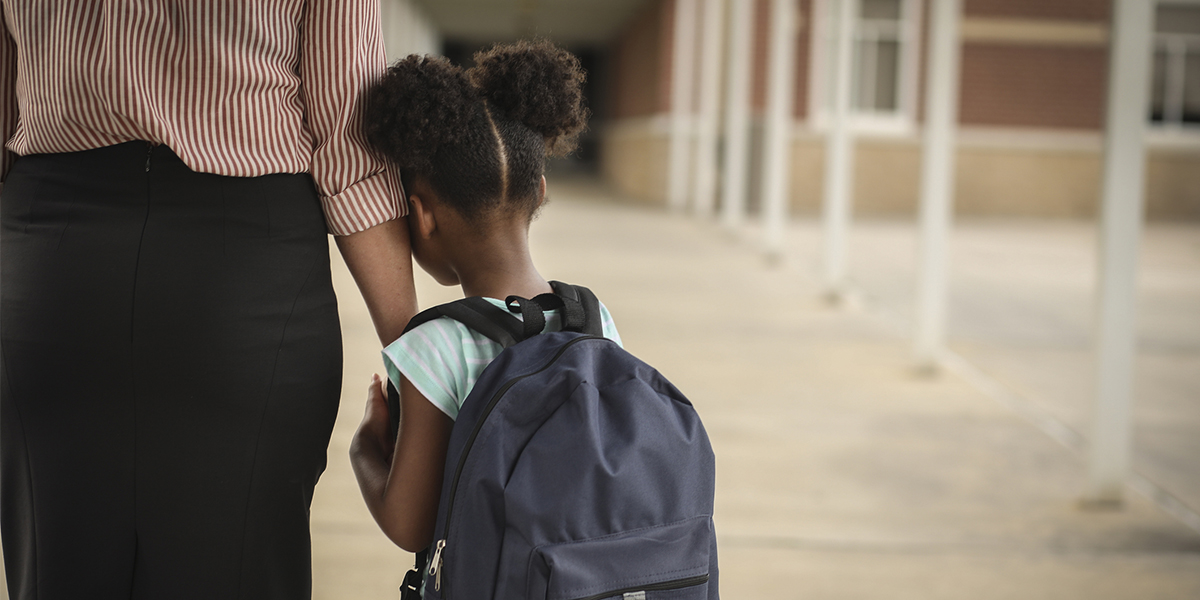 Child hugging parent's arm headed into school