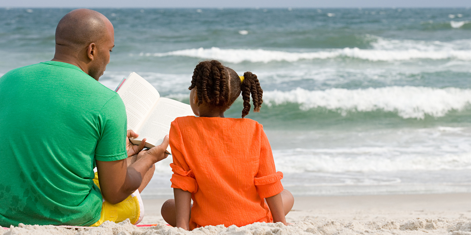 A father and daughter reading at the beach