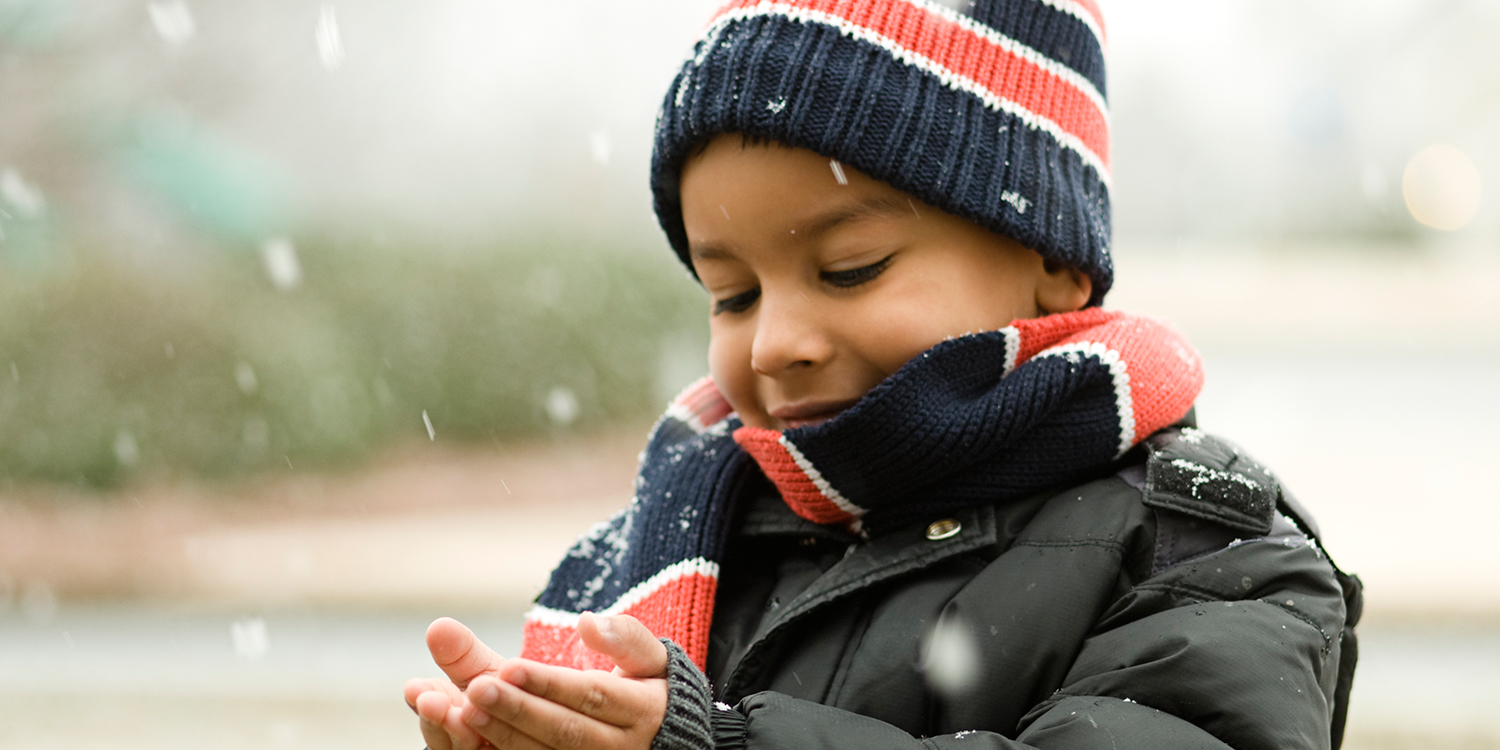 boy in winter coat, hat, scarf catching snowflakes