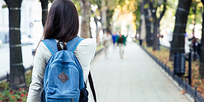 Female student from the rear, walking down long campus pathway
