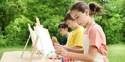 Three children painting on easels set up outside