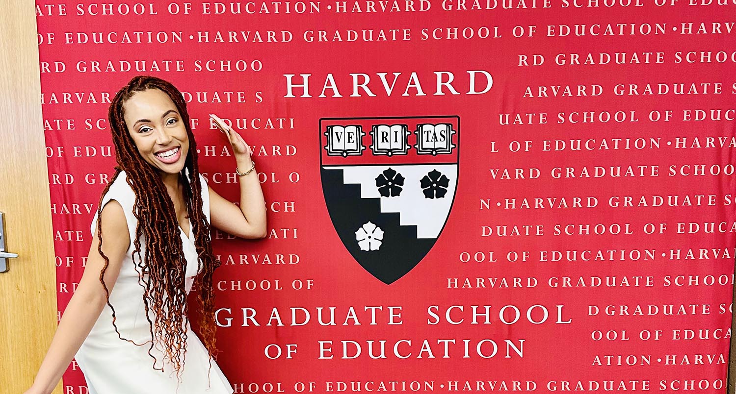 Inella Ray posing in front of a red HGSE banner