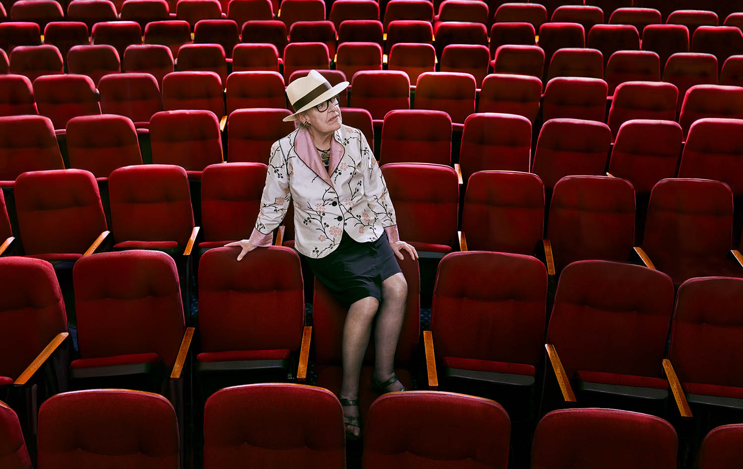Photo of Catherine Snow sitting alone in an auditorium with red chairs