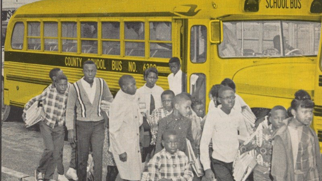 A black and white photo of Black students getting off a school bus in the 1970s