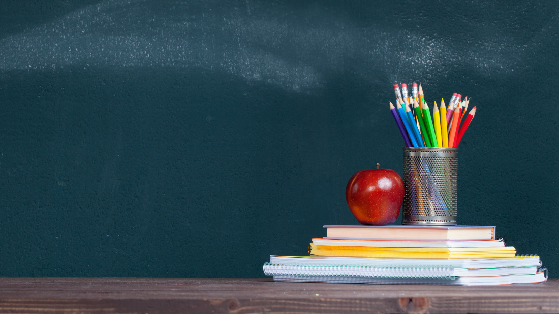 Pencil tray and an apple on notebooks on school teacher's desk