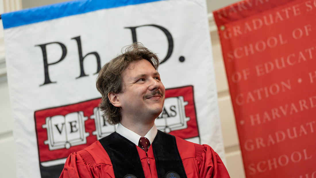 Ph.D. student at robing in front of banner