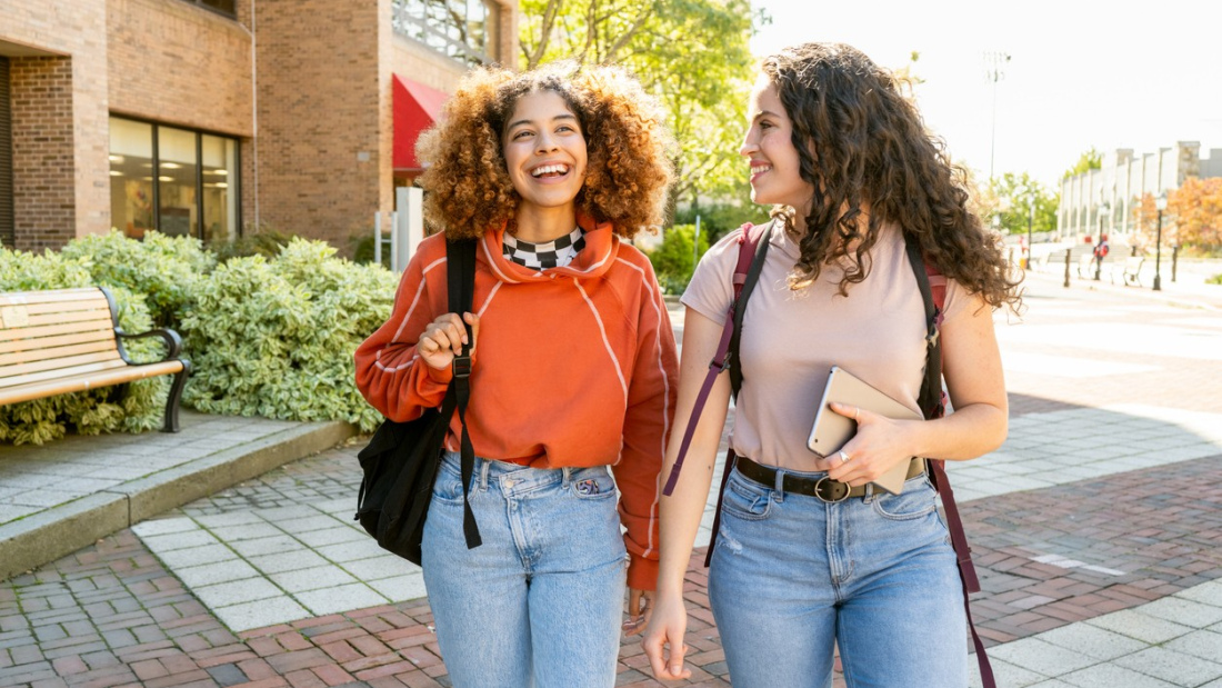 Two Gen Z students smile and walk together on campus