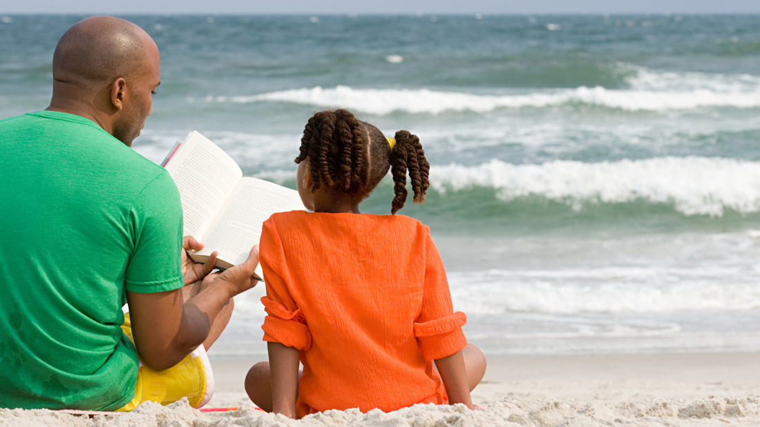 A father and daughter reading at the beach