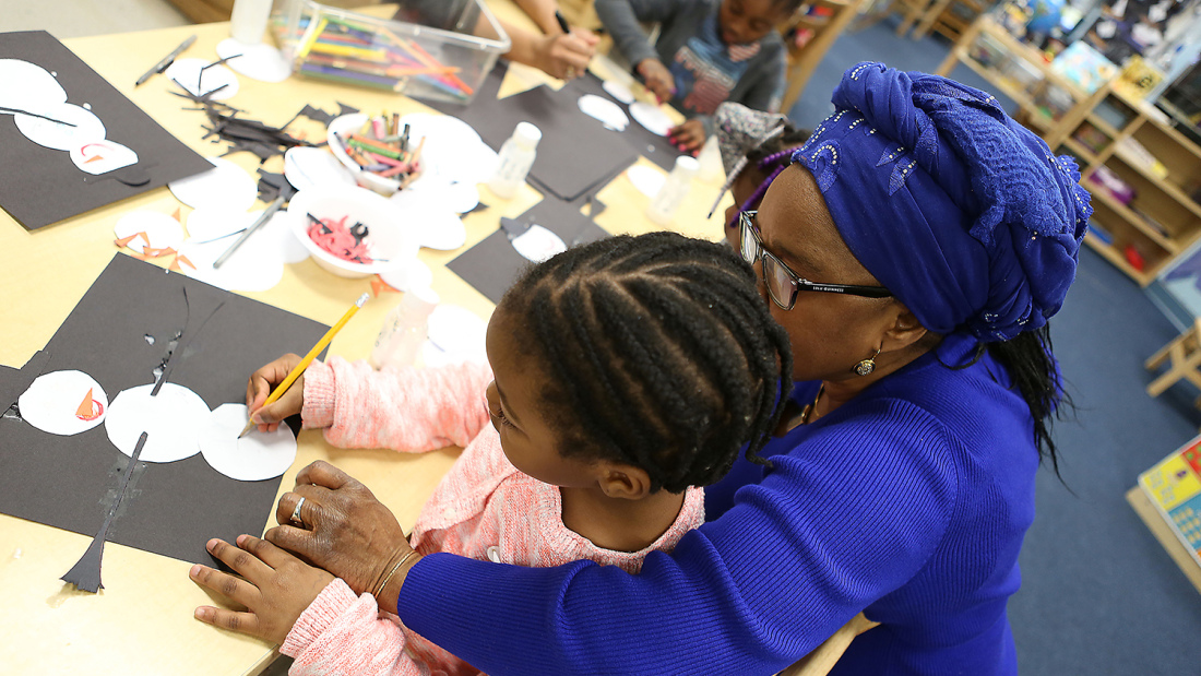 preschool teacher helping young girl with her drawing
