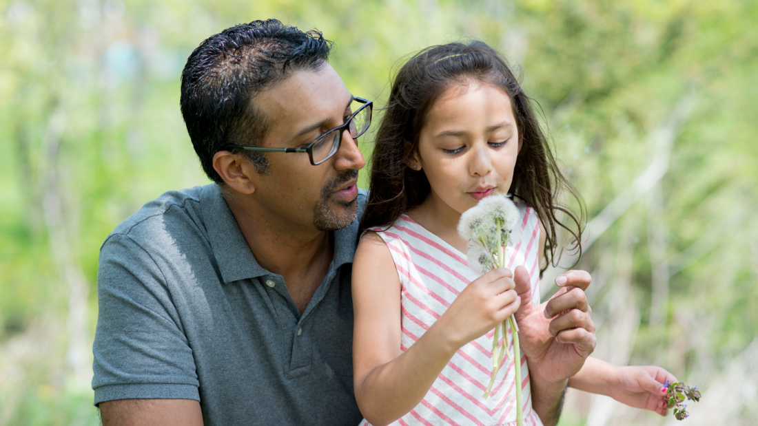 An image of a girl and her father blowing a dandelion 