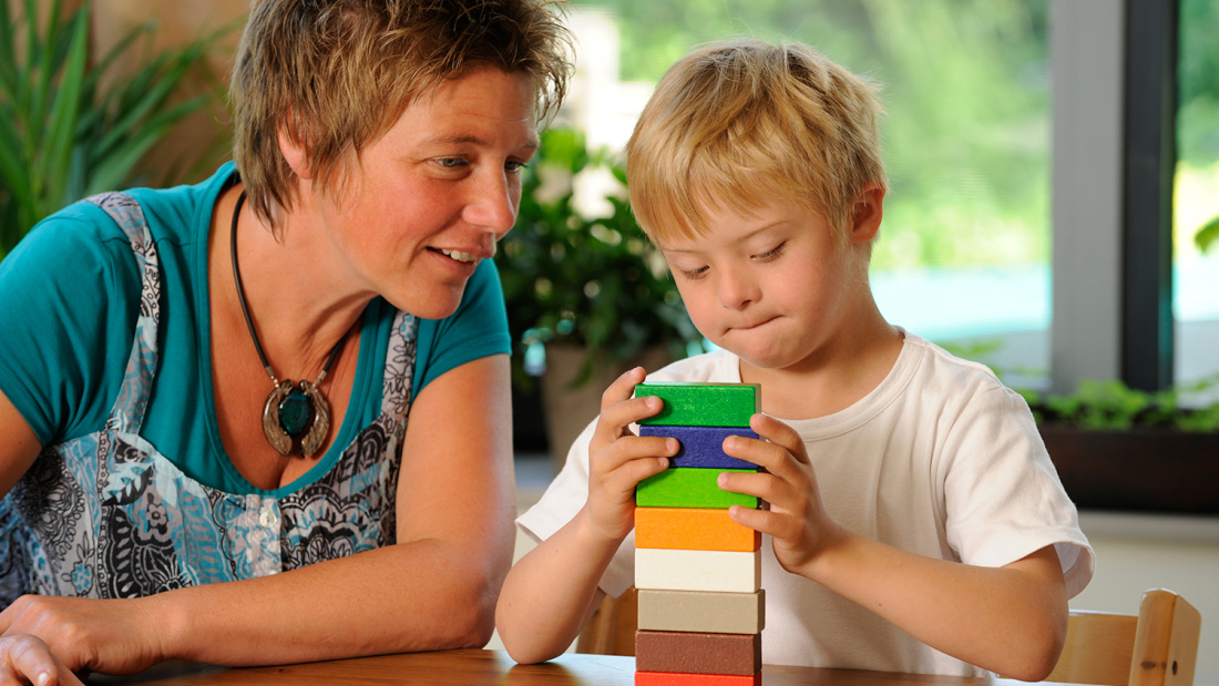 Teacher with a young child building a block tower
