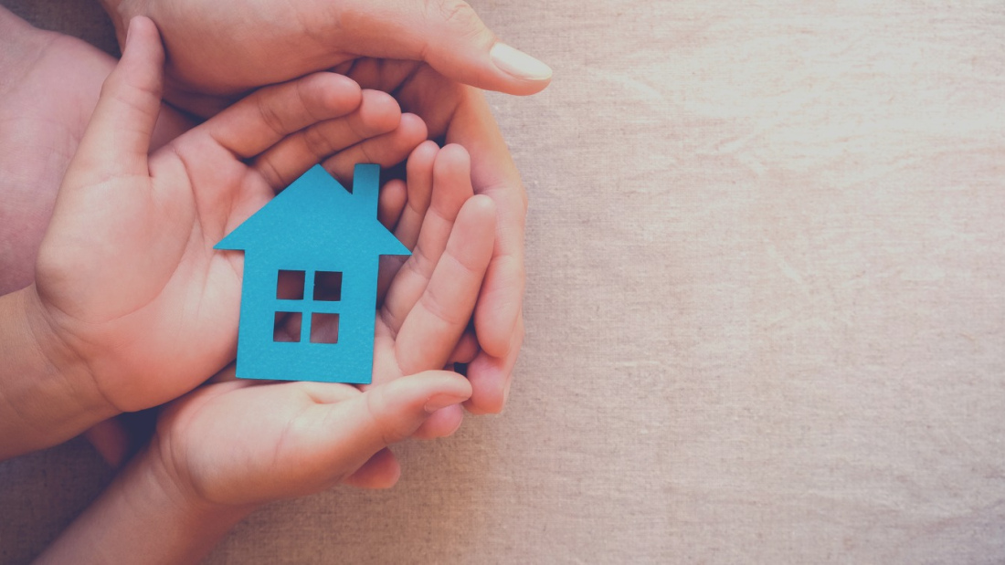 small blue schoolhouse in child's hand, cupped by adult hand