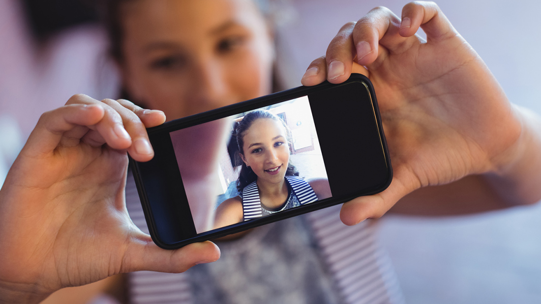 A photo of a teen holding up a phone with a picture of herself