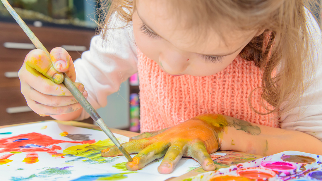 preschool-age girl using watercolors to paint outline of her hand