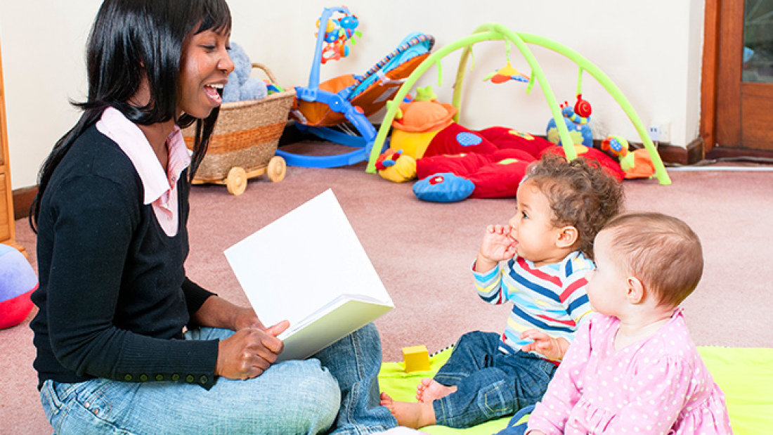 Home daycare teacher reading to two infants