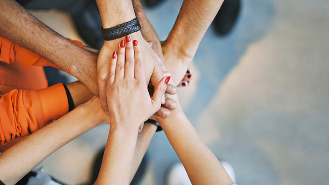A circle of hands placed on top of one another, suggesting unity