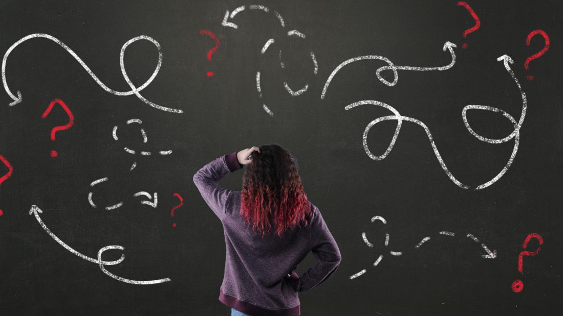 Photo of a teenaged girl looking confused in front of a blackboard with many arrows
