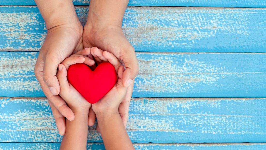 A photo of adult hands and child hands holding a heart on a blue table