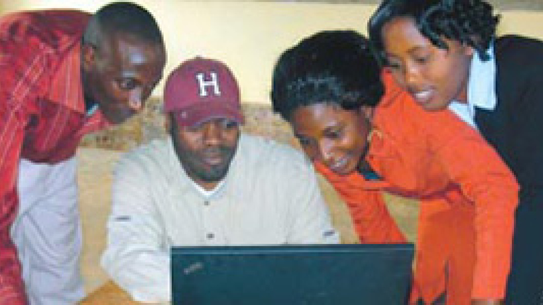 Haynes (baseball cap) demonstrates to teachers how to use one of the new computers at Crimson Academy in Rwanda