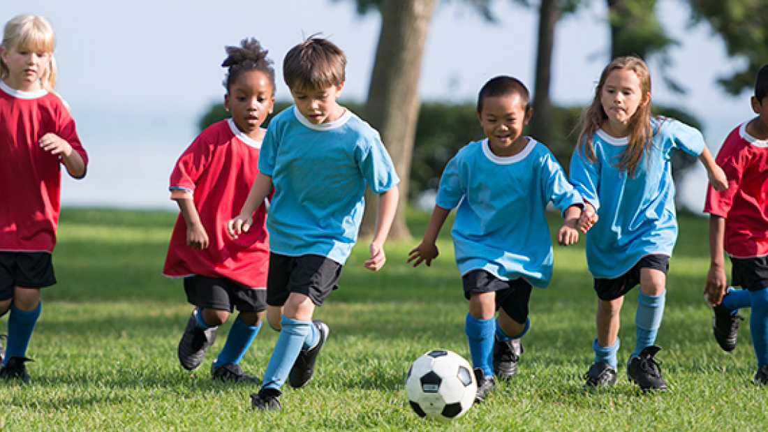 young kids on a field running after soccer ball 