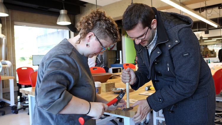 A man and woman work together on an innovative project on a wooden table with hammers.