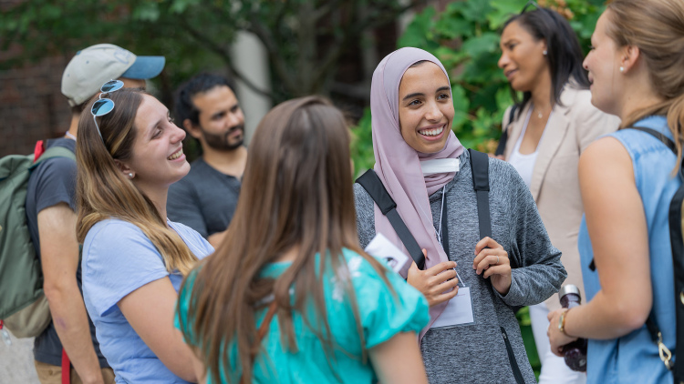 A group of students and faculty smile while discussing things outside.