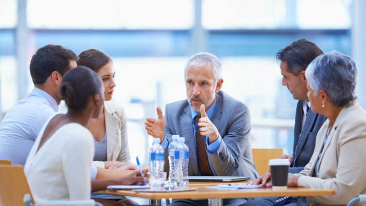 A man in a suit shares ideas with colleagues at a meeting table.