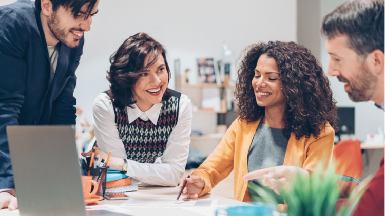 Four educators collaborate at a table using a laptop and paper