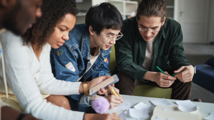 Four students collaborate at a table, all writing on paper.