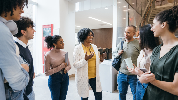 Teacher talks to diverse group of students in school lobby