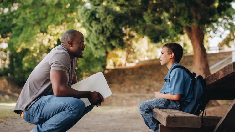 Counselor talking to a young school kid outside class, providing support and encouragement.