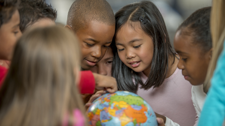A group of elementary age students are learning the places of the world by looking at a globe.