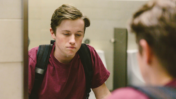 Photo of young boy looking sad in school bathroom mirror