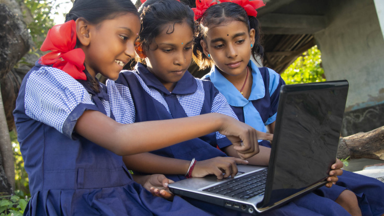 Three schoolgirls from India look at materials on a laptop