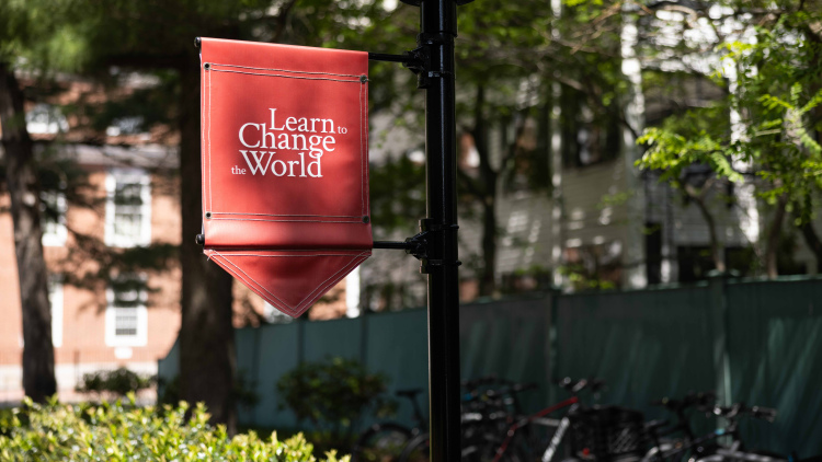 Crimson flag that reads "learn to change the world" on campus at HGSE