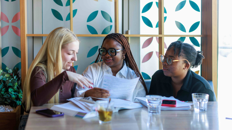 Three happy colleagues sitting in a coffee shop and collaborating