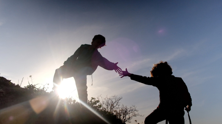 A student extending a hand to help another student climb a hill
