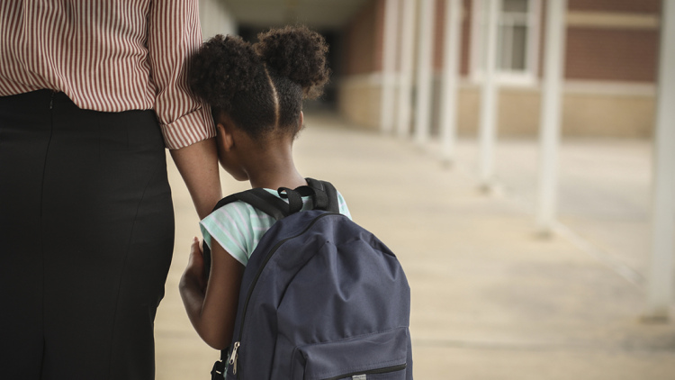 Child hugging parent's arm headed into school
