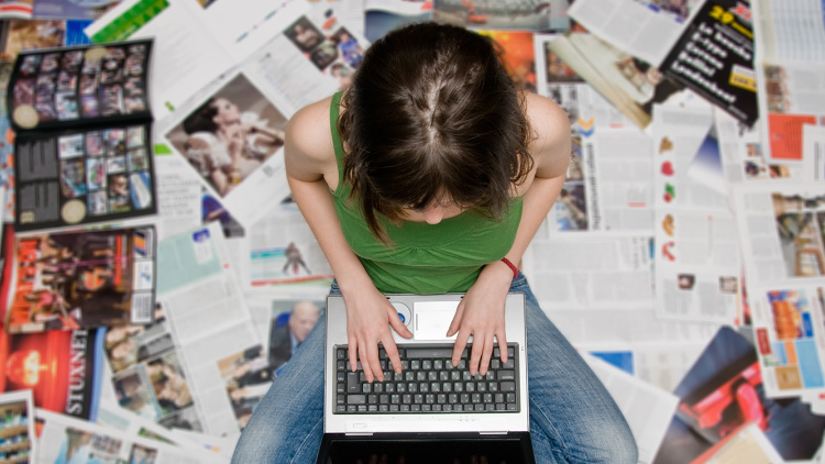 Teen sitting on newspapers with laptop