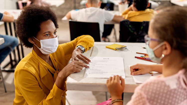 Teacher in classroom with student, both in masks