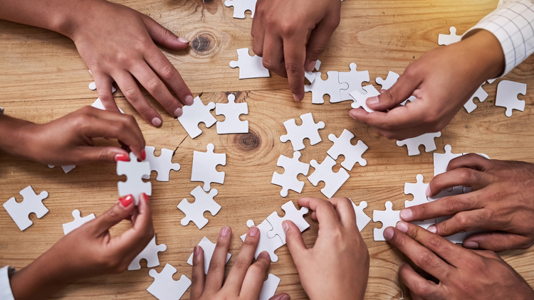 Seen from above, hands of a group of people putting together jigsaw puzzle