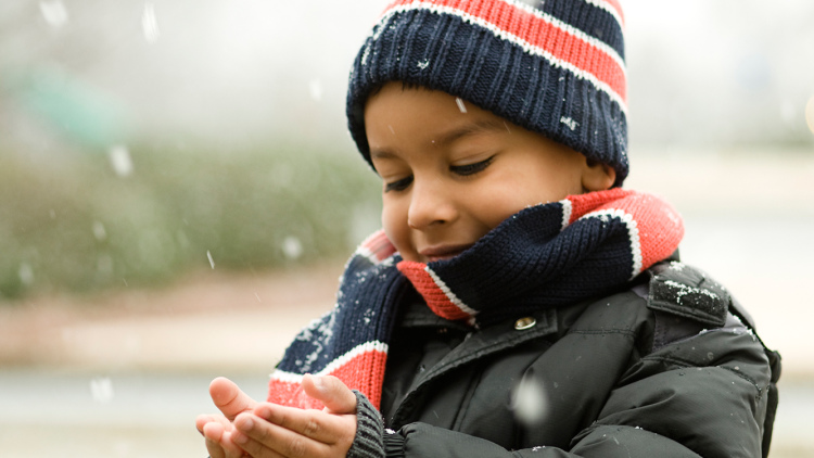 boy in winter coat, hat, scarf catching snowflakes
