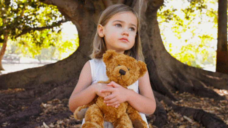 A small girl holds onto a teddy bear