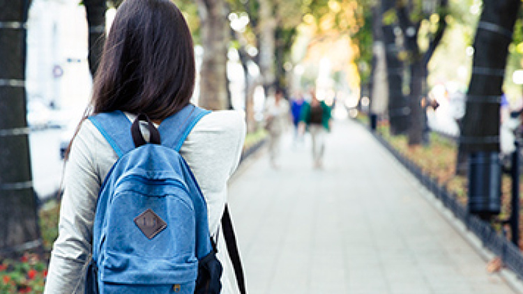 Female student from the rear, walking down long campus pathway