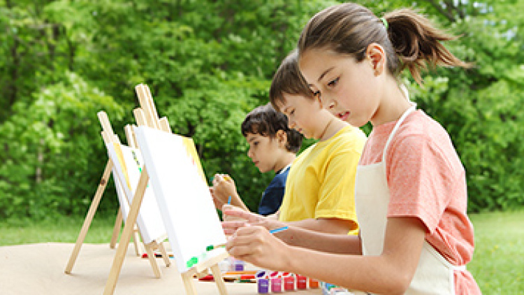 Three children painting on easels set up outside