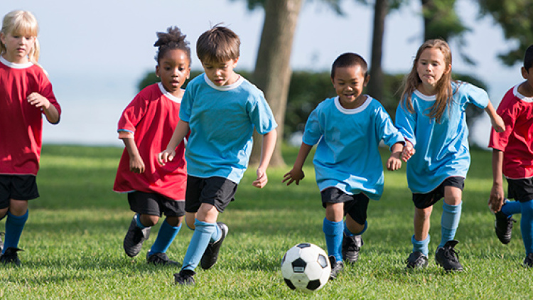 young kids on a field running after soccer ball 