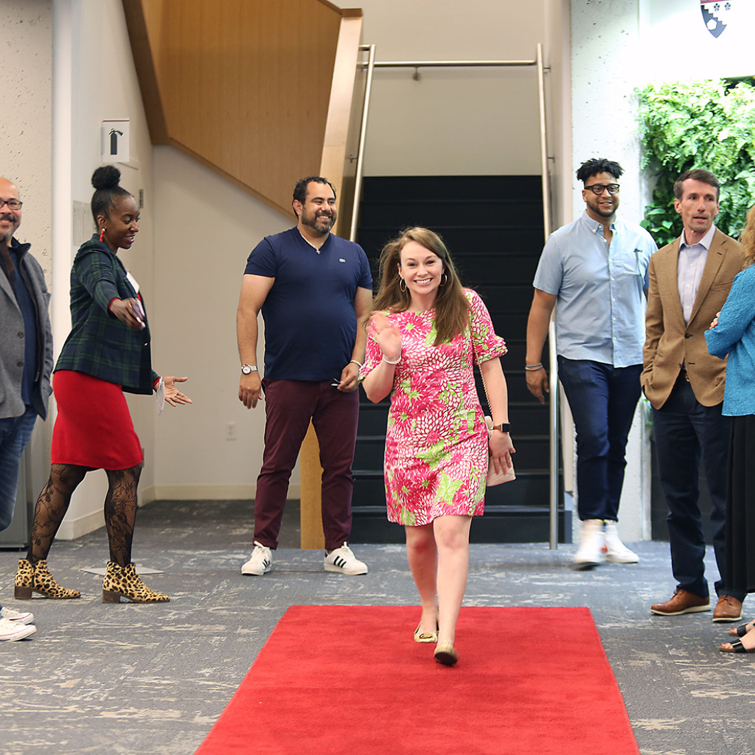 A woman walks down a red carpet in the Gutman Conference Center with the encouragement of her peers