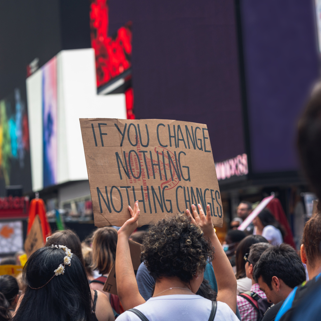 Someone holds up a poster that reads "if you change nothing, nothing will change" during a protest in a city.