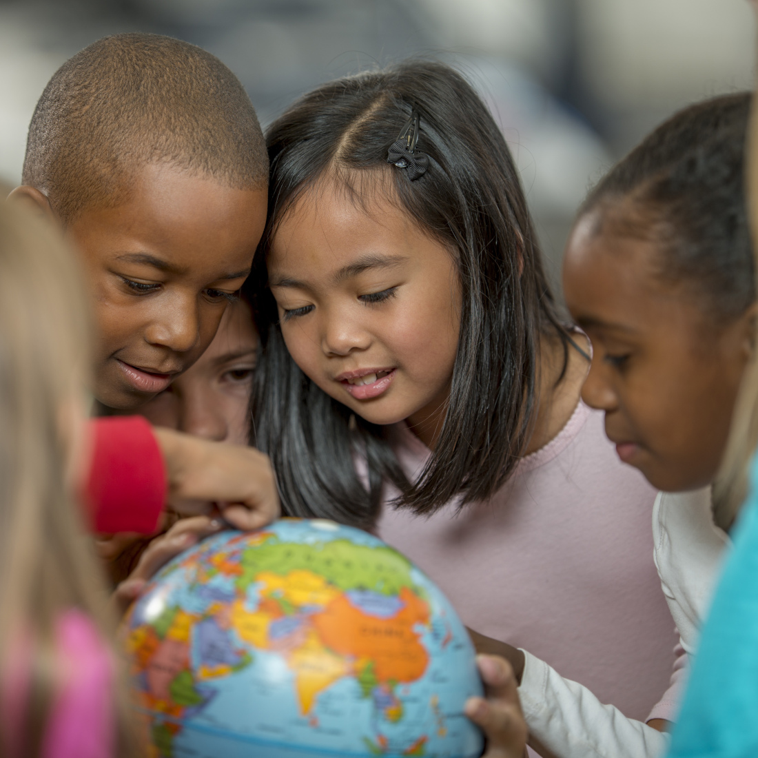 A group of elementary age students are learning the places of the world by looking at a globe.